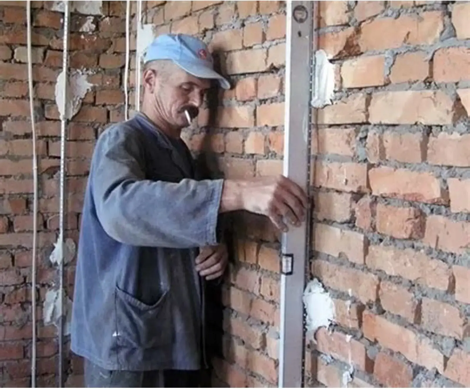 Рабочий выставляет штукатурный маяк по уровню на кирпичной стене